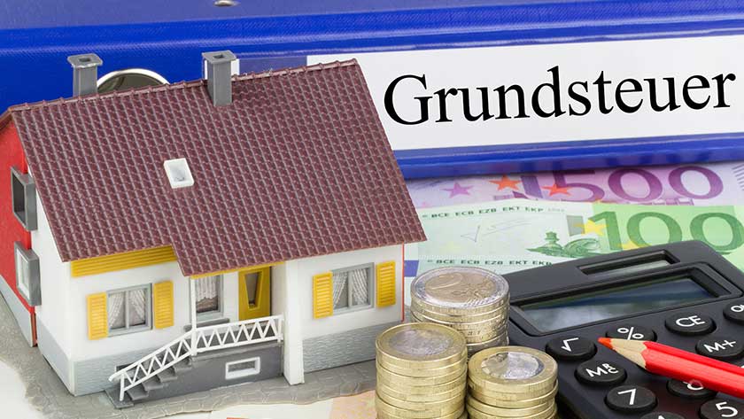 Foto von einem Modelhaus, Münzen sowie einem Taschenrechner zur Veranschaulichung der Grundsteuerreform 2022
